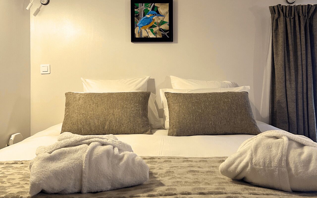Une chambre d’hôtel avec un lit, deux oreillers, une couverture et un tableau au mur.