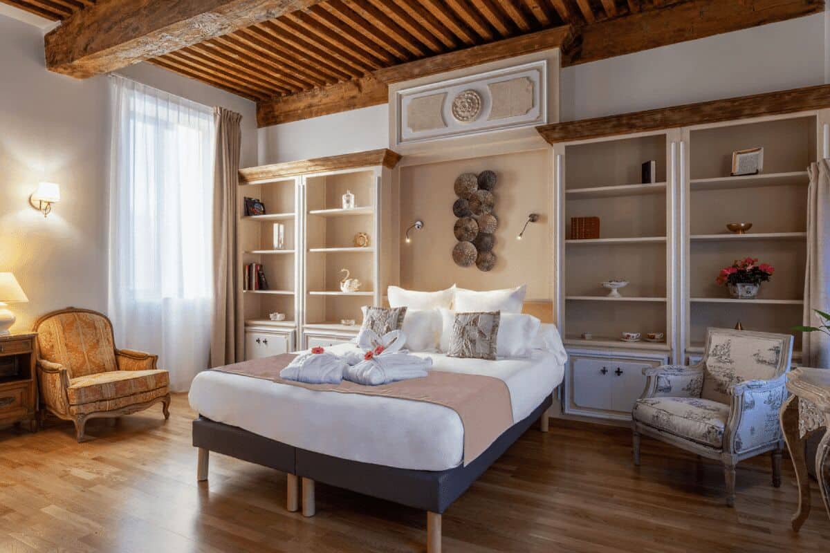 Un dormitorio espacioso con una cama grande, suelo de madera, estanterías integradas y un clásico candelabro.