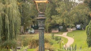 Un lampadaire traditionnel, installé dans un jardin, avec un sentier et des arbres en arrière-plan.