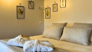 Una cama bien hecha con un albornoz blanco encima, una pared de color claro e impresiones botánicas enmarcadas.
