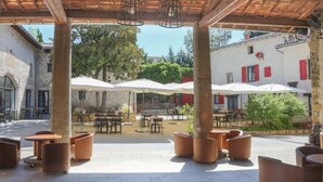 Un patio al aire libre con mesas y sillas, vigas de madera en el techo y sombrillas para dar sombra.