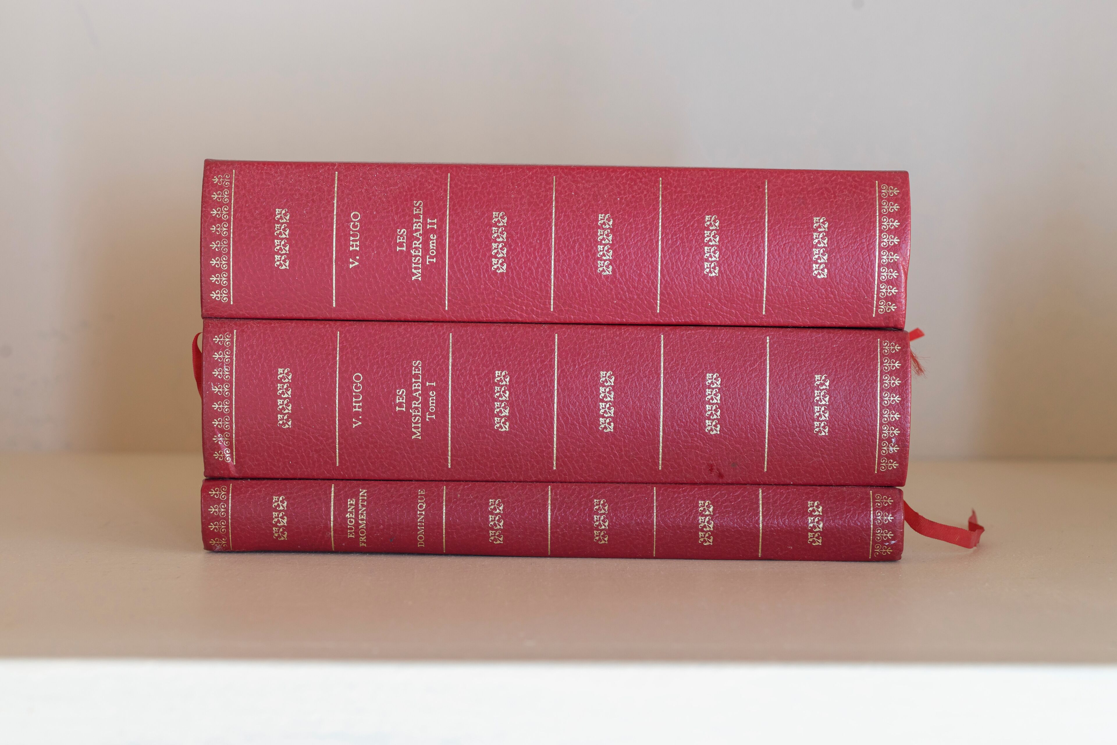Une pile de trois livres rouges dont les titres sont écrits en lettres dorées, posée sur une surface blanche.