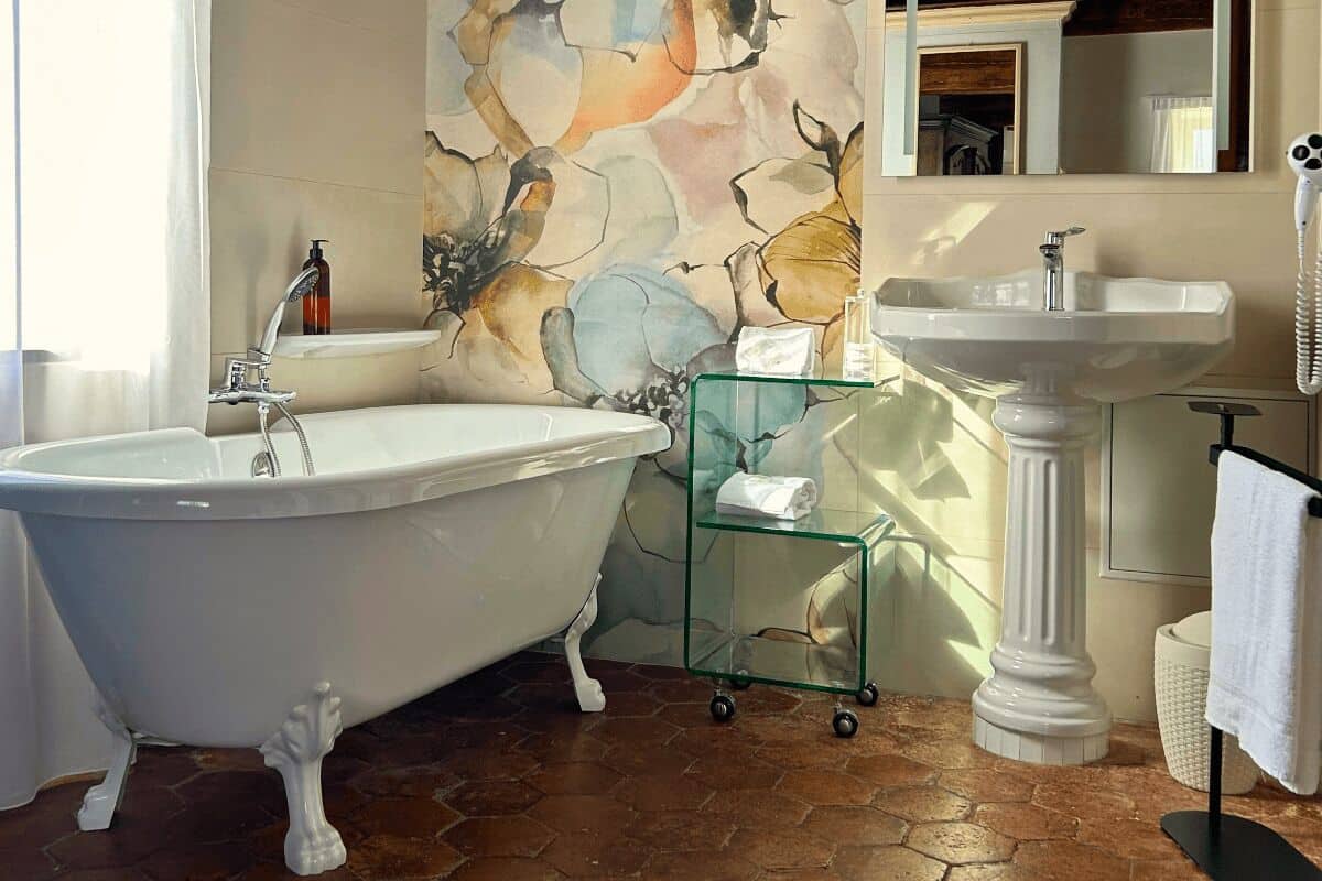 Un baño con una bañera independiente, un estante de vidrio con artículos de aseo, un lavamanos pedestal y un espejo.