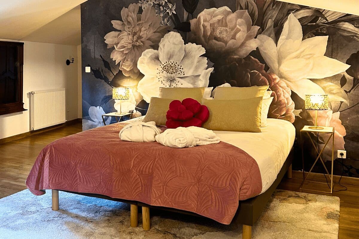 Un dormitorio con una cama grande, decoración floral en la pared, dos lámparas de noche y un radiador.