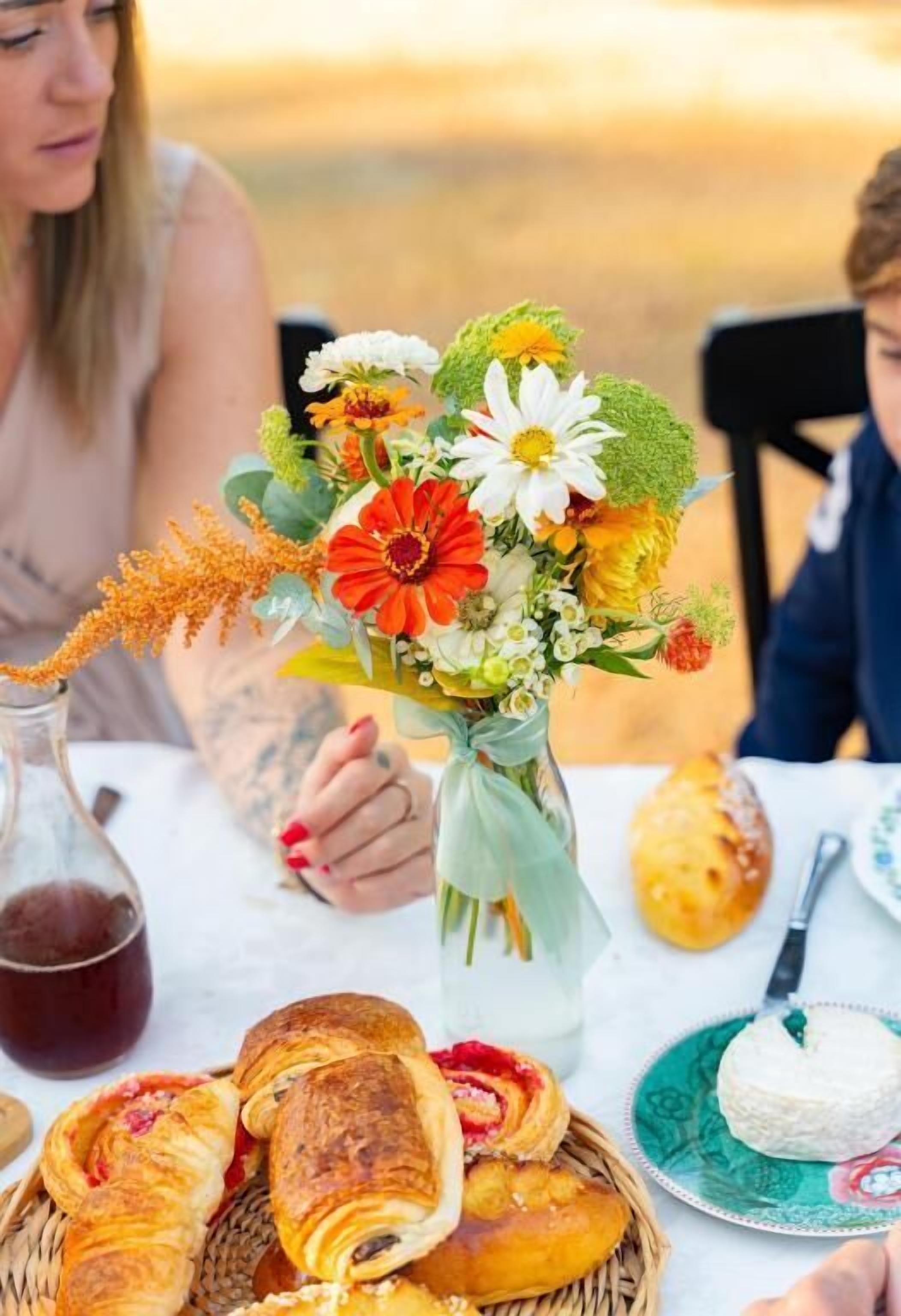 Una mesa con un arreglo floral, pasteles y una botella de bebida.