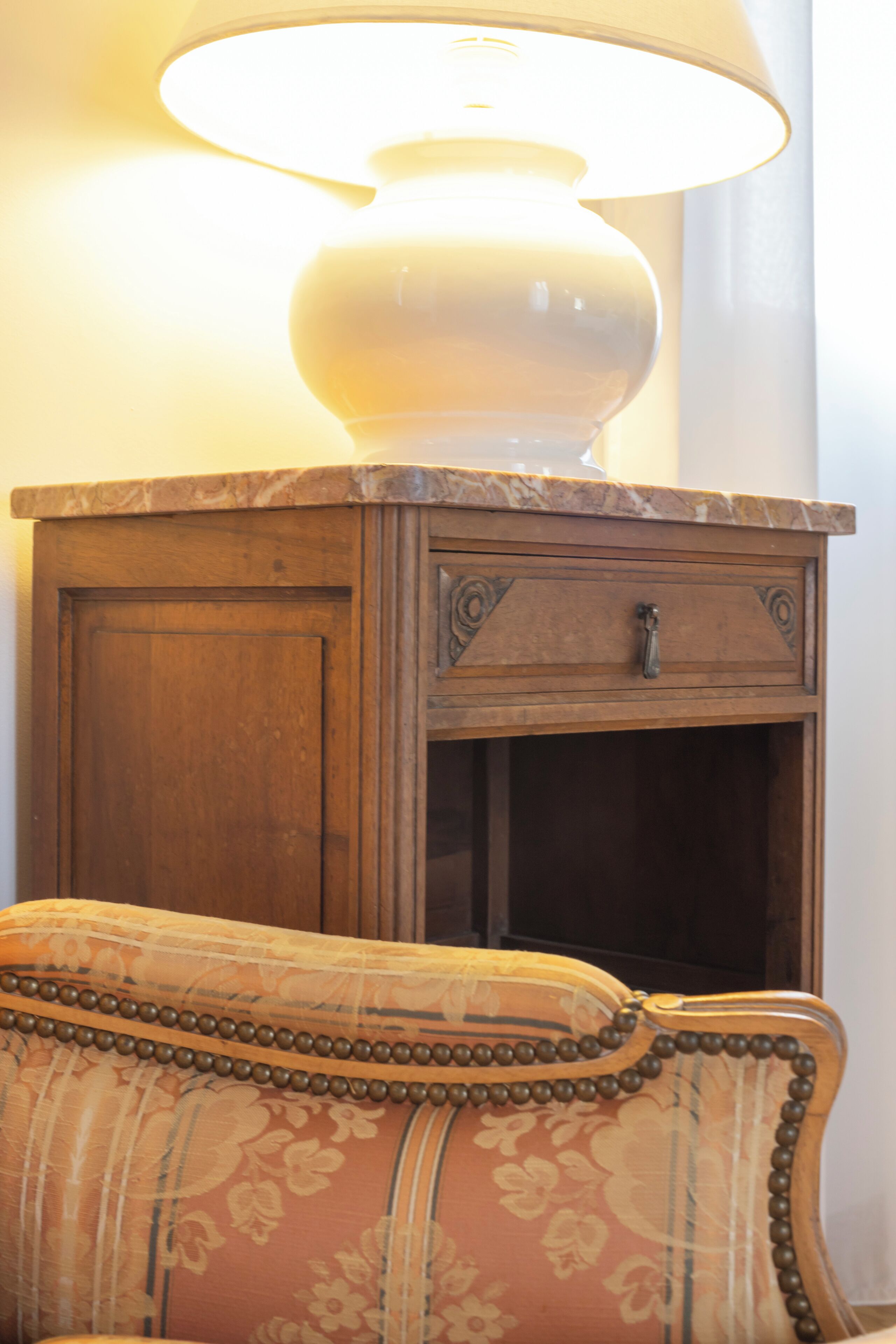 Un armario de madera con una lámpara encima, un sillón con cojín estampado con motivos florales y una puerta de madera con manija.
