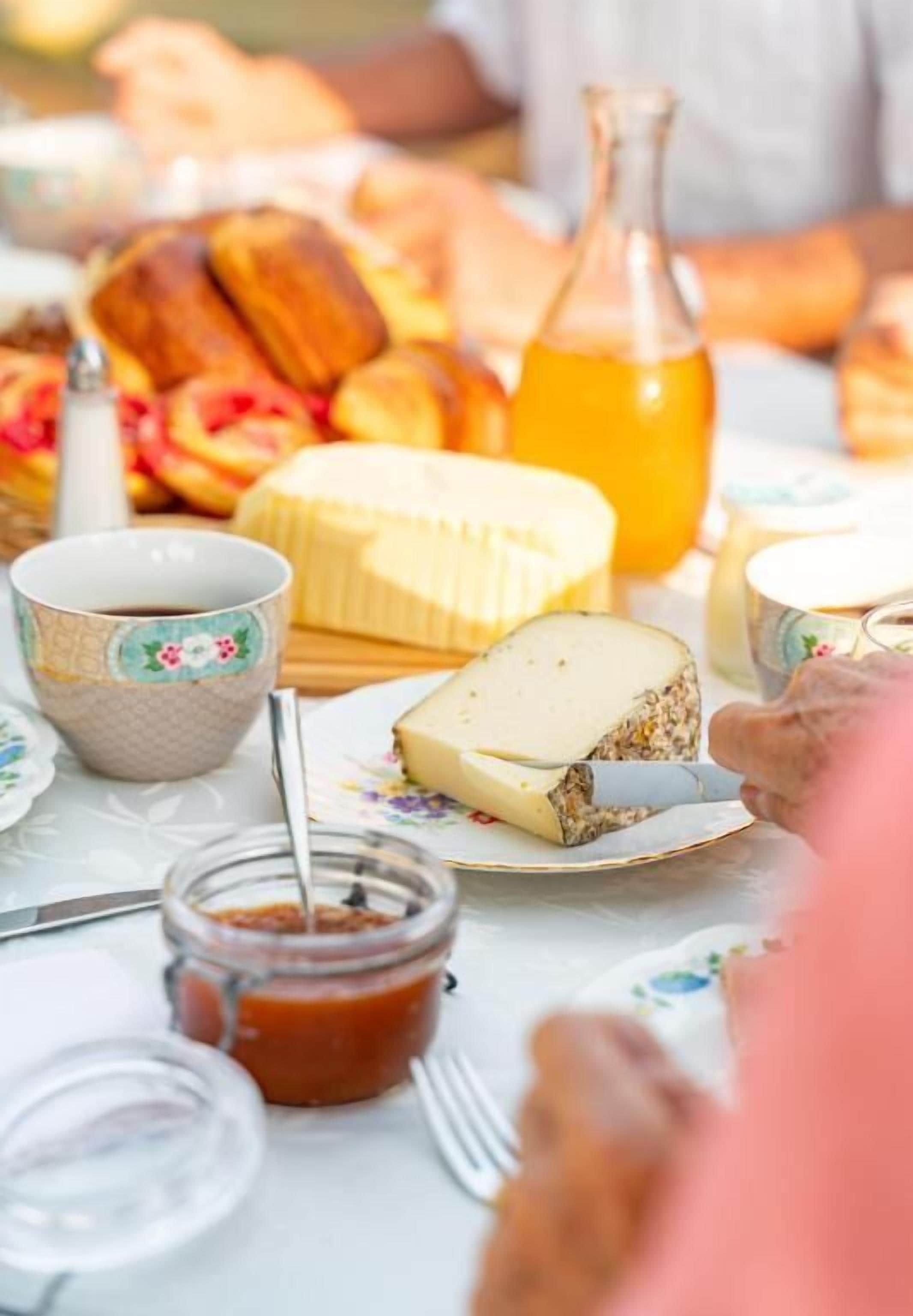 Une table sur laquelle on trouve une variété d’aliments, notamment une grande tranche de fromage, du pain et une bouteille de jus d’orange.
