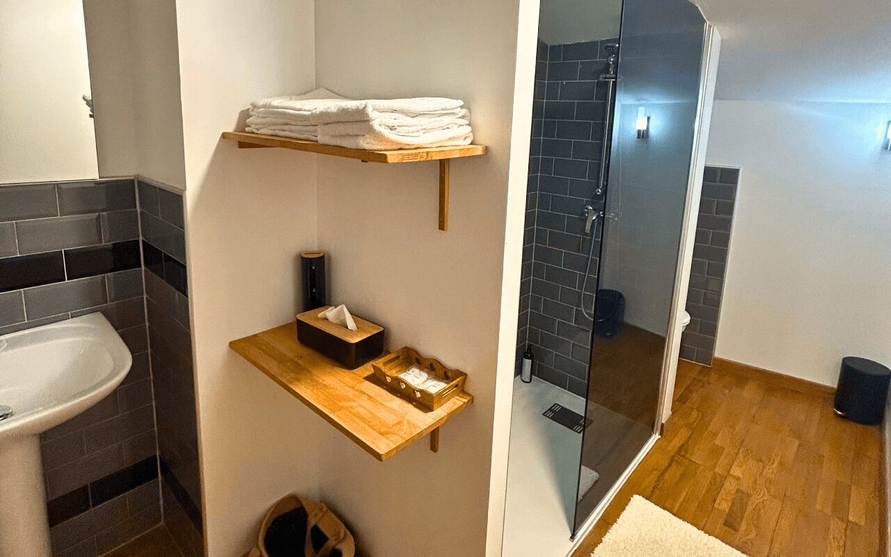 Un baño con lavamanos, espejo, toallero y cabina de ducha con mampara de vidrio.