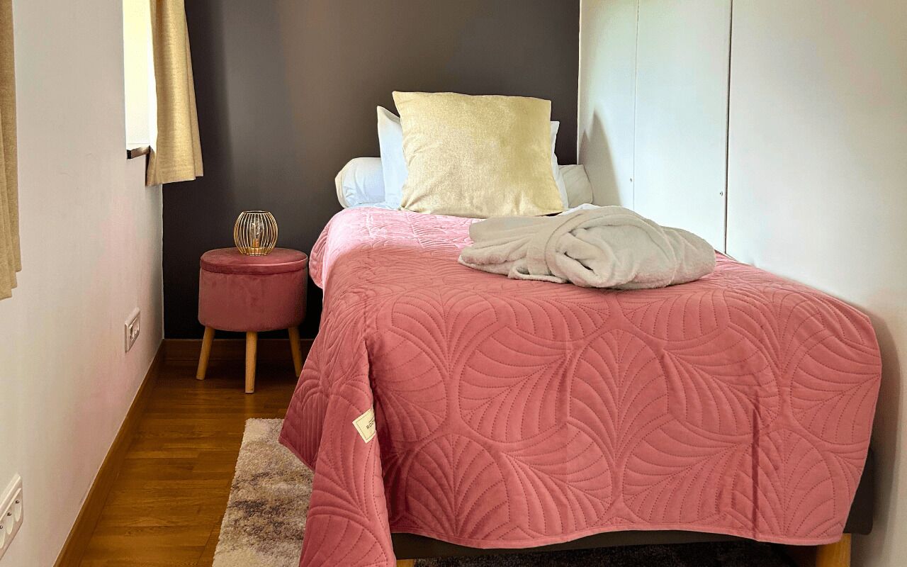 A bedroom with a bed, a small round table, a red stool, and a white wardrobe.