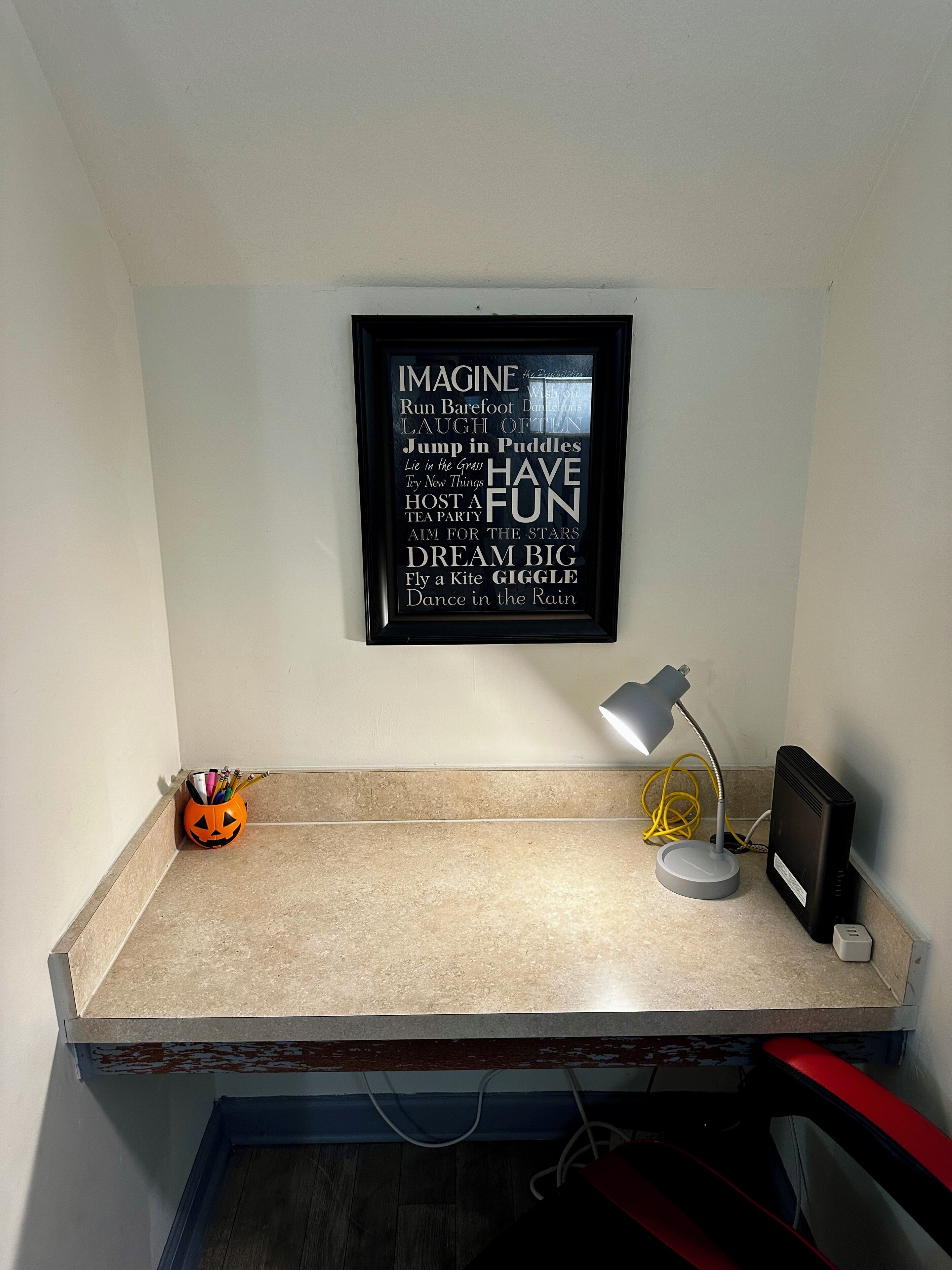 A desk with a framed motivational poster, a lamp, and a computer on a tiled floor.