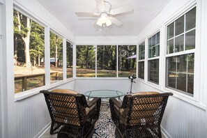 A sunroom with a glass table and wicker chairs, large windows, and a ceiling fan. - 6.5 Acres - Remodeled Private Ranch. EV Charger. Fire pit. Comfy and calm. (Lilburn)