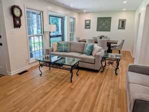 A living room with a glass coffee table, a sofa with decorative pillows, a dining area with a table and chairs, and a clock on the wall. - 6.5 Acres - Remodeled Private Ranch. EV Charger. Fire pit. Comfy and calm. (Lilburn)