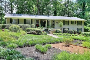 A two-story house with a front porch, surrounded by well-maintained landscaping and trees. - 6.5 Acres - Remodeled Private Ranch. EV Charger. Fire pit. Comfy and calm. (Lilburn)