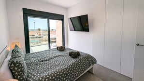 Un dormitorio con cama, televisor, puerta corrediza de vidrio y vistas al exterior.