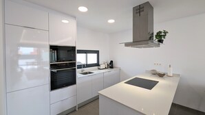 Una cocina moderna con armarios blancos, una estufa negra, una ventana y una campana extractora empotrada.