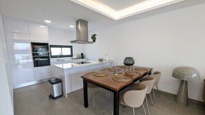 Una cocina moderna con armarios blancos, una isla central y un comedor con mesa y sillas de madera.