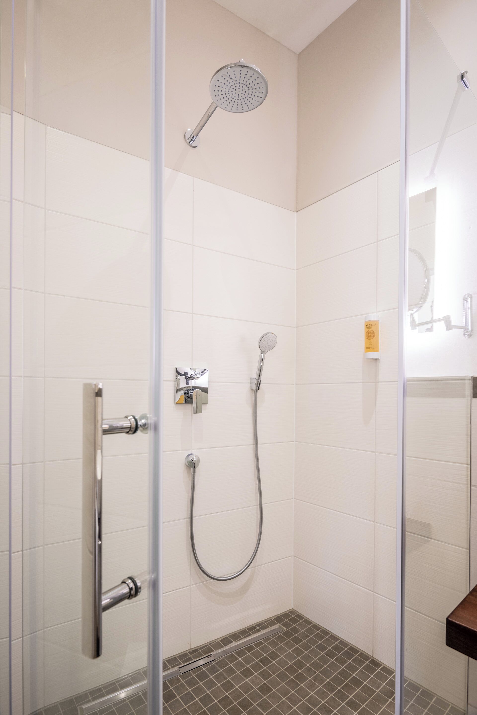A glass-enclosed shower with a handheld showerhead and a wall-mounted faucet.