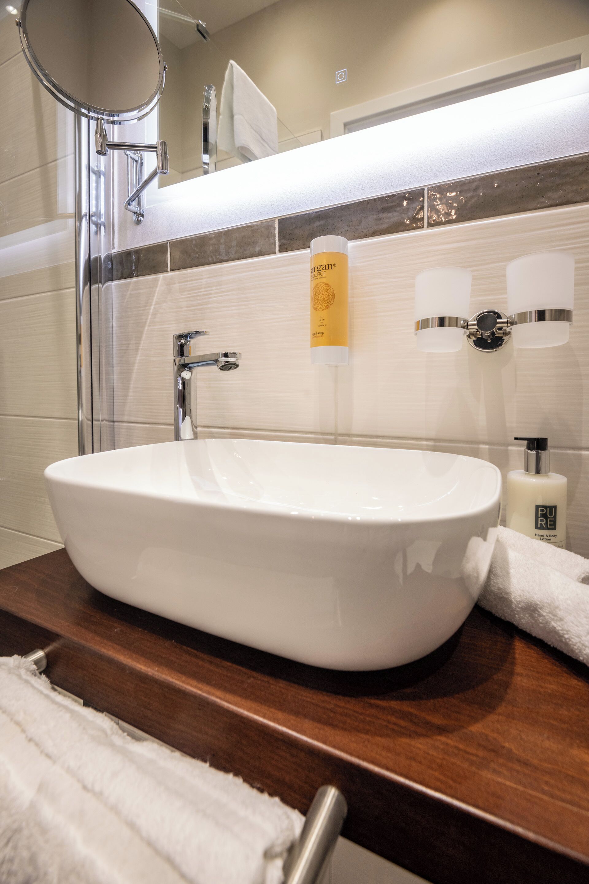Un baño con un lavamanos ovalado blanco, un espejo, un perchero para toallas y una botella de jabón Pure.