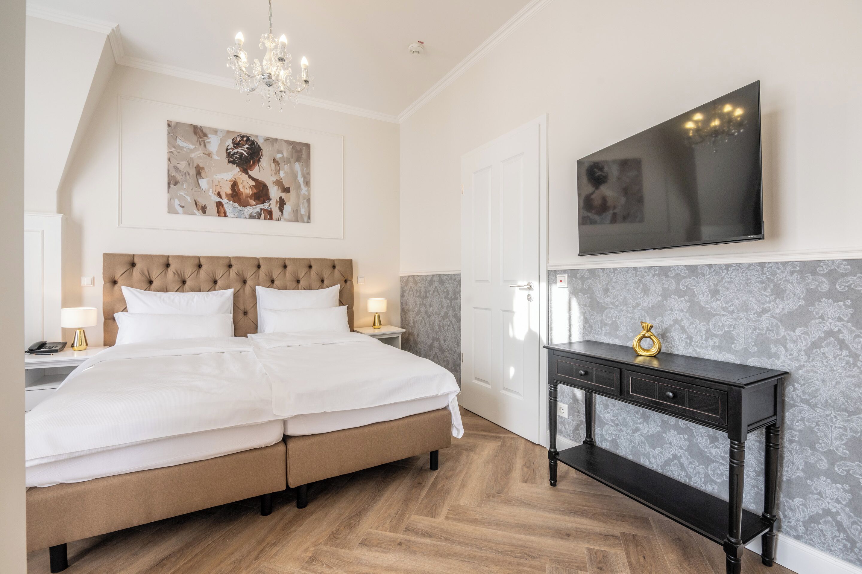 A bedroom with a large bed, a chandelier, a flat-screen TV, and a console table.
