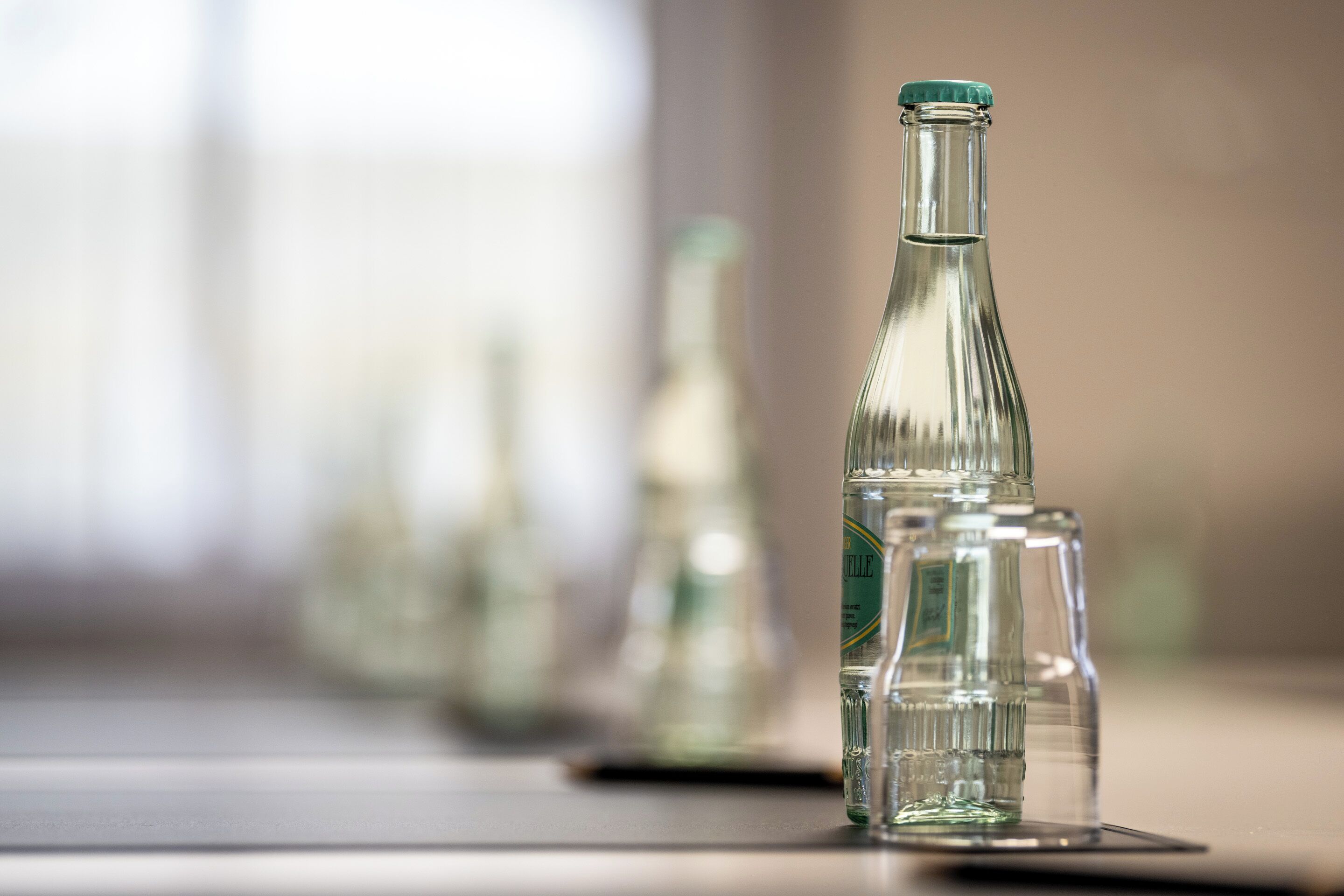 Una botella de vidrio transparente con tapón verde sobre una superficie reflectante.