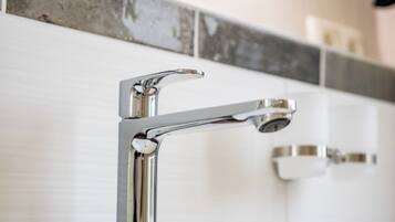 Ein modernes Badezimmer mit einem chromfarbenen Wasserhahn, einem weißen Waschbecken und einer gefliesten Rückwand.