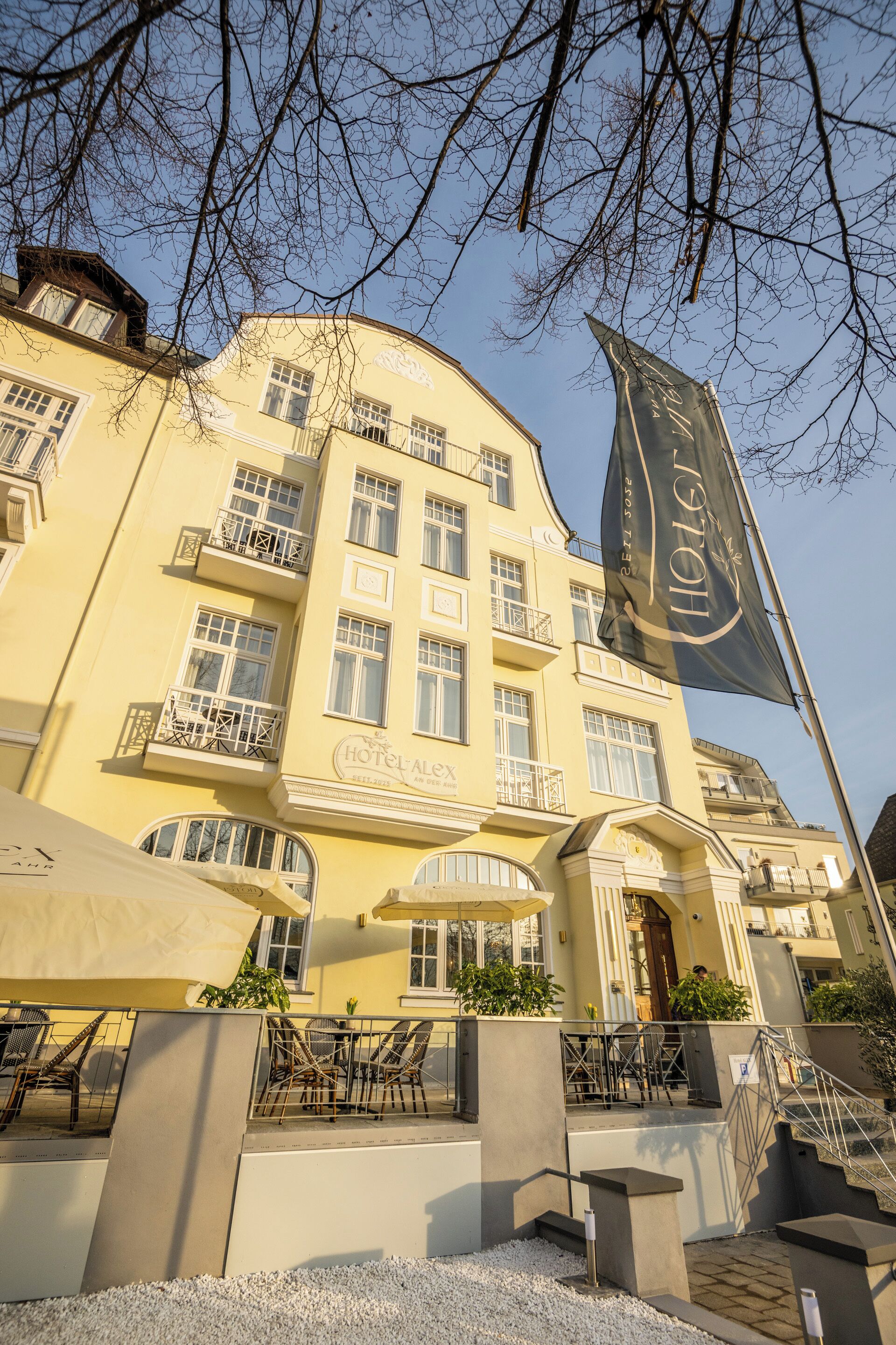Un hotel con fachada amarilla, varios balcones y asientos al aire libre.
