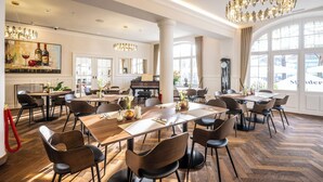 A spacious dining area with multiple tables and chairs, large windows, and a grand chandelier.