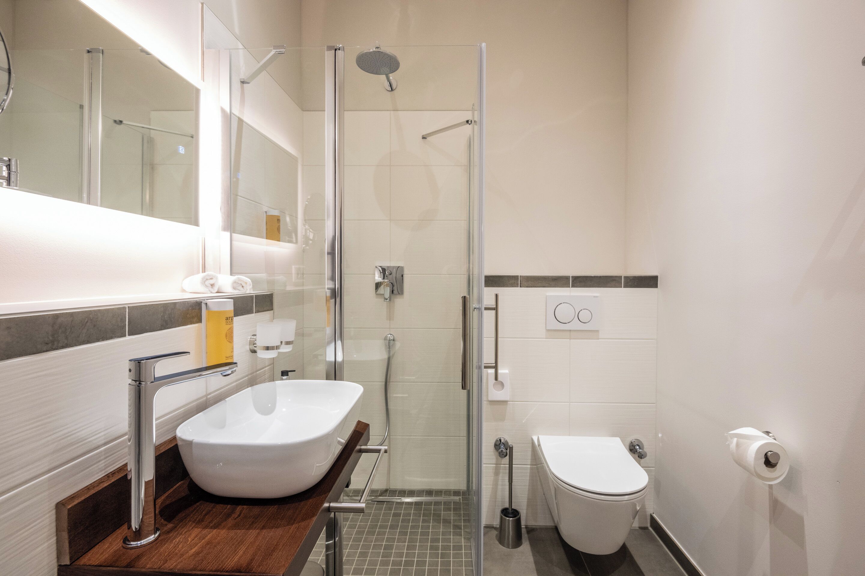 Un baño moderno con ducha de vidrio, lavamanos blanco y un inodoro.