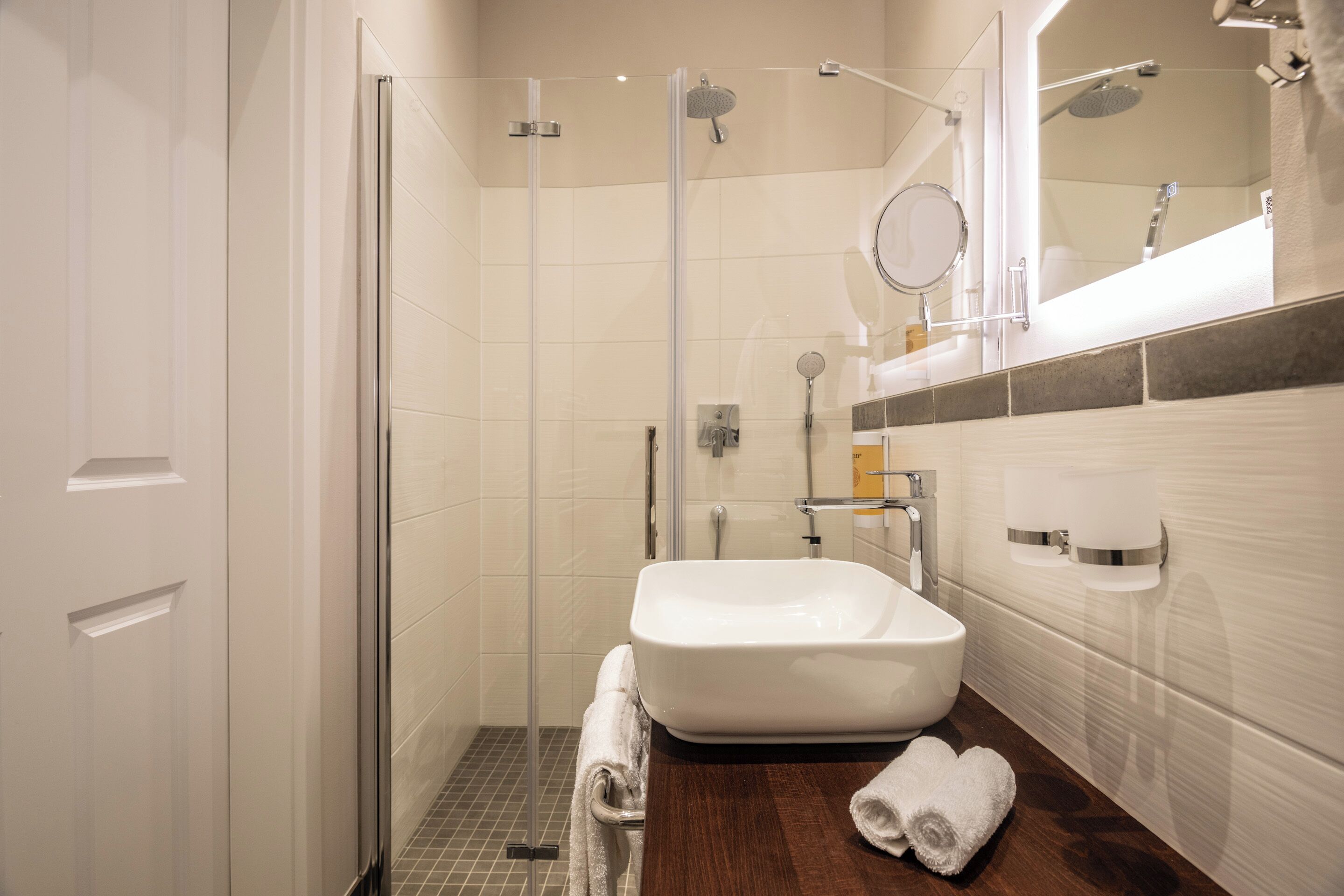 A modern bathroom with a glass-enclosed shower, a white sink, and a wooden vanity.