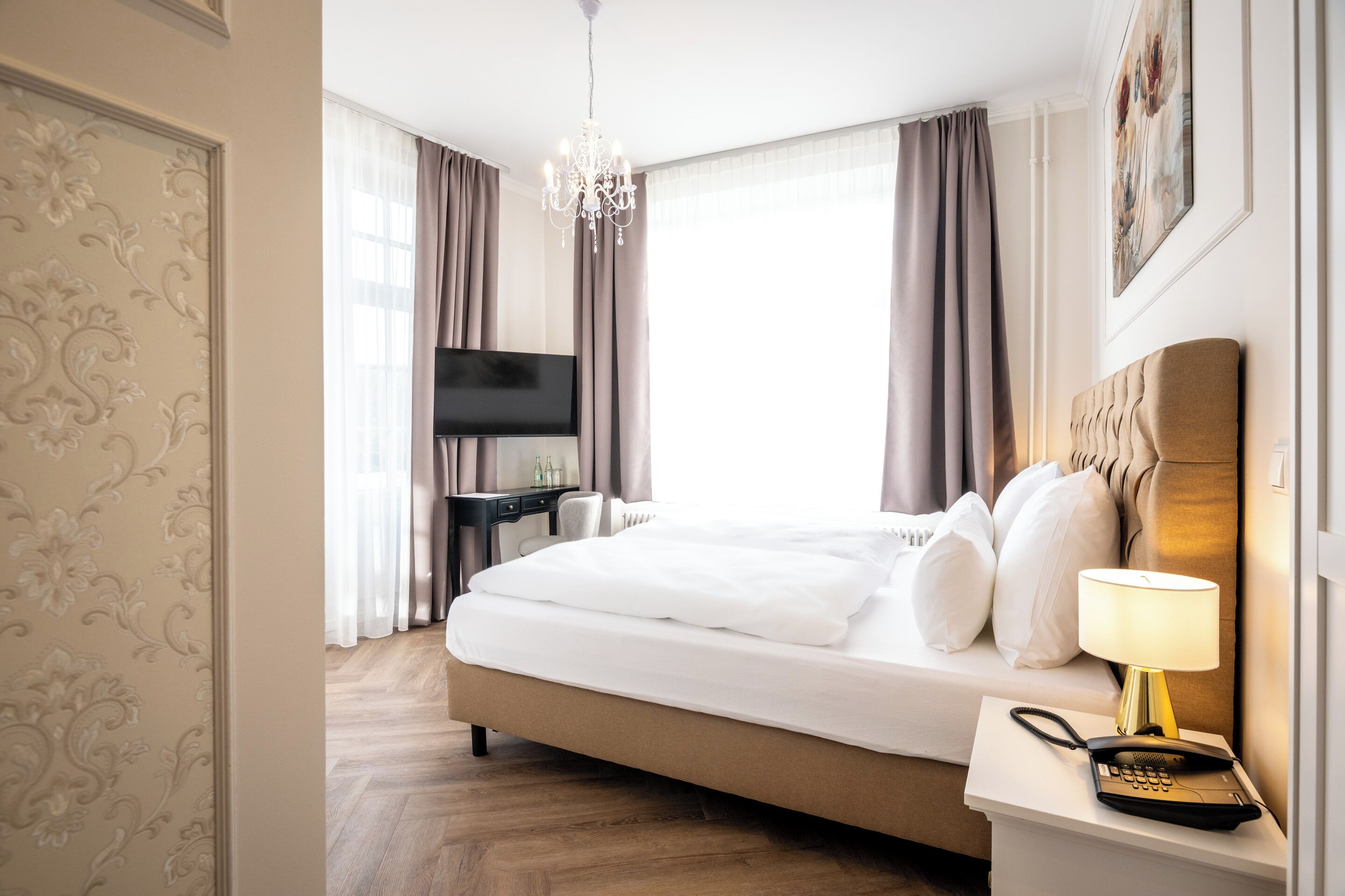 Une chambre d’hôtel avec un grand lit, une lampe de chevet, un téléphone et un téléviseur posé sur un bureau.