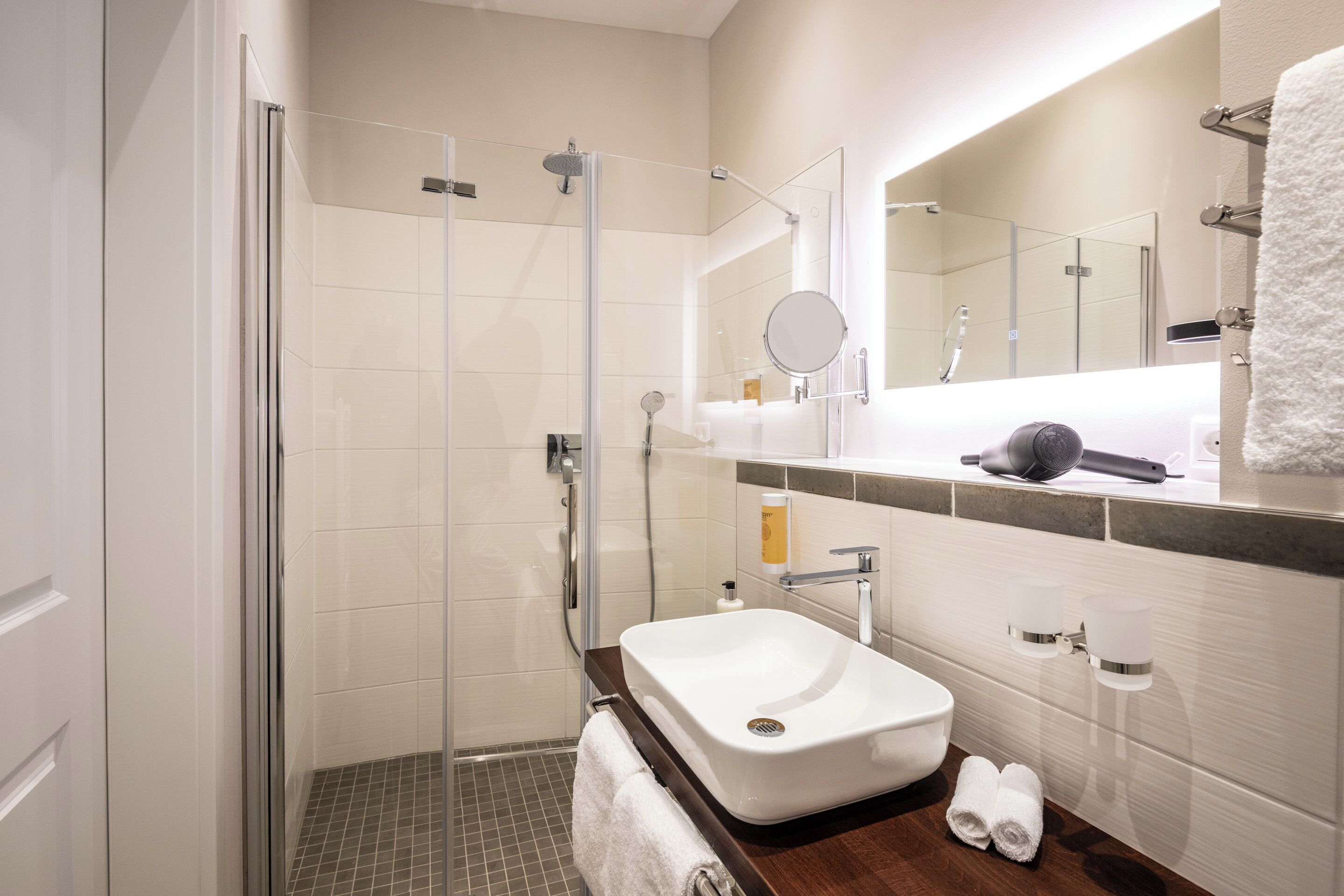 A modern bathroom with a glass-enclosed shower, a white sink, and a large mirror.