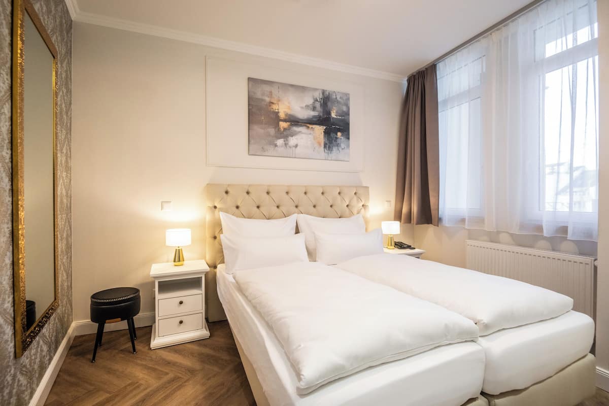 A hotel room with a large bed, a bedside table with a lamp, a small stool, and a large mirror.
