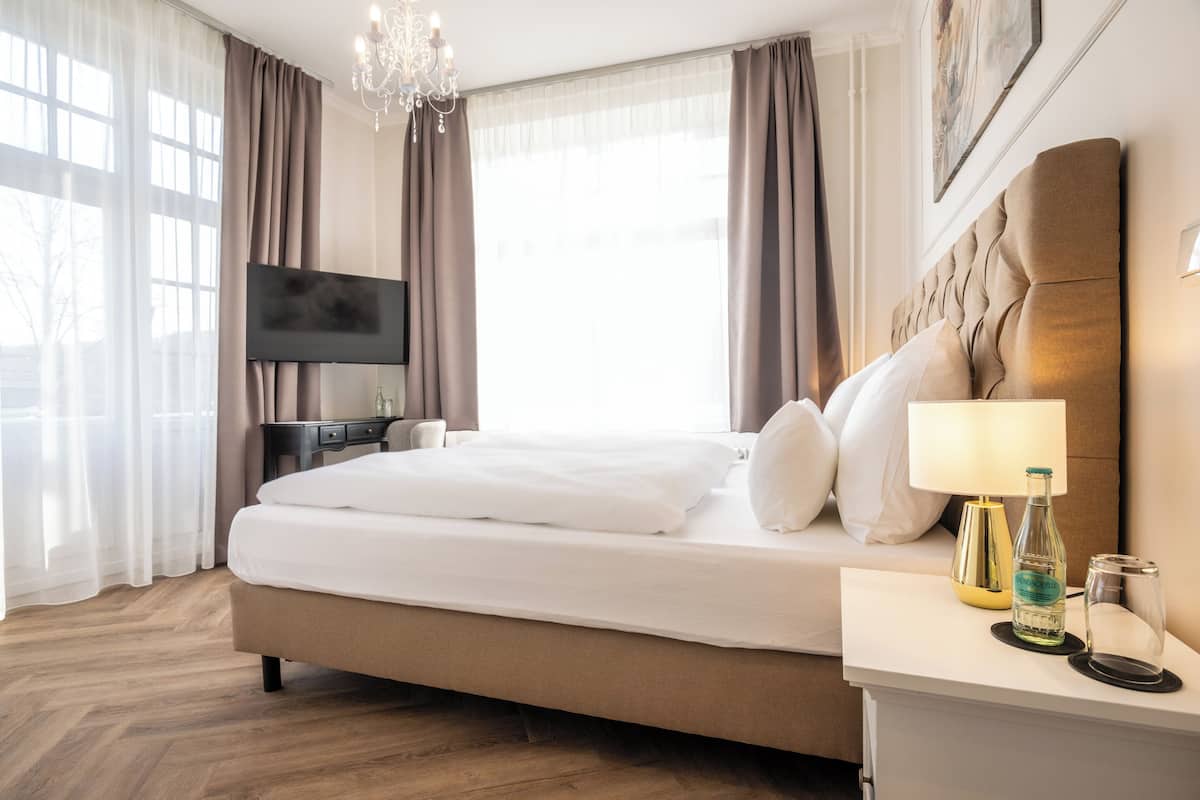 A hotel room with a large bed, a flat-screen TV, a bedside table with a lamp, and a bottle of water.
