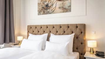 Habitación de hotel con cabecera capitonada, dos camas blancas, un cuadro en la pared y lámparas de noche.