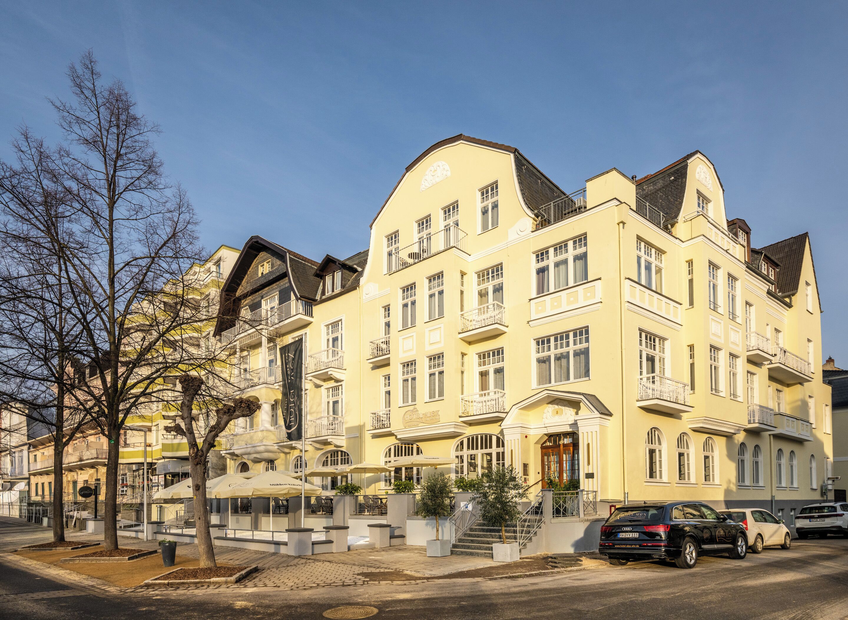 A multi-story hotel with a yellow facade, balconies, and a central entrance with steps.