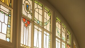 A room with large windows featuring stained glass, a view of the street outside, and a door leading to an outdoor area with tables and chairs.