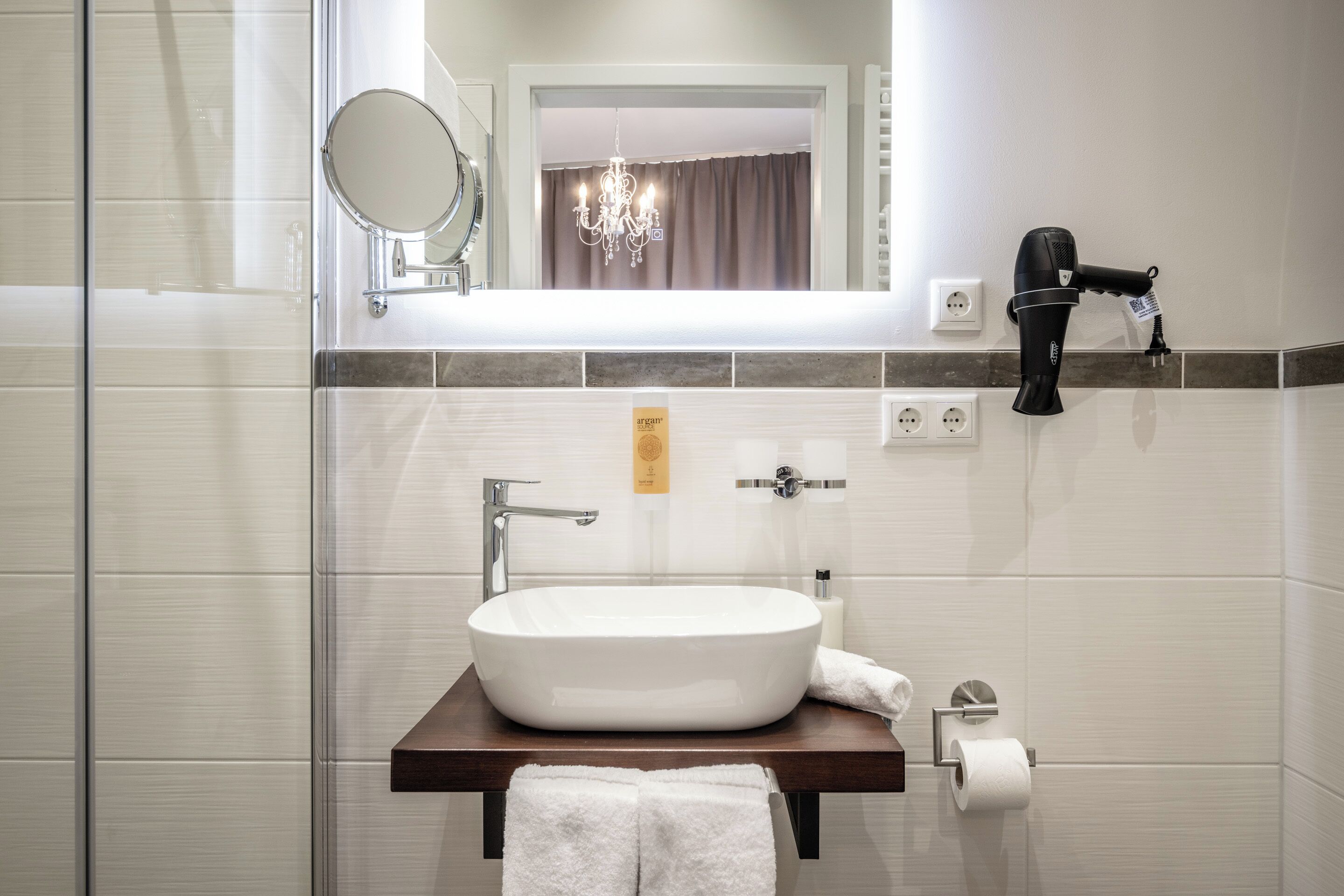 A bathroom with a white sink, a mirror, a towel rack, a hairdryer, and a chandelier.