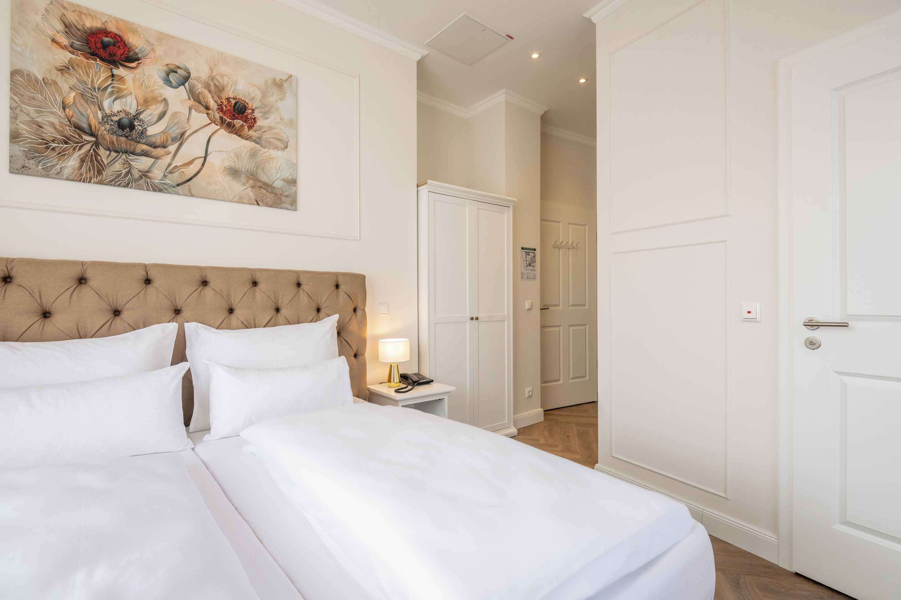 A hotel room with a large bed, a tufted headboard, a bedside table with a lamp, and a painting on the wall.