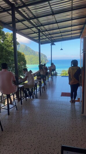 A covered outdoor seating area with a view of the ocean and mountains. - The View Hostel (Ko Phi Phi)