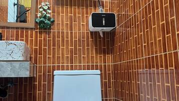 Ein Badezimmer mit Toilette, einem Mülleimer, einem Regal mit Pflanze und einem an der Wand befestigten Lufterfrischer.