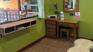 A corner room with a green wall, a wooden desk, a mirror, a vanity, a window with curtains, and a view of an outdoor seating area. - The View Hostel (Ko Phi Phi)