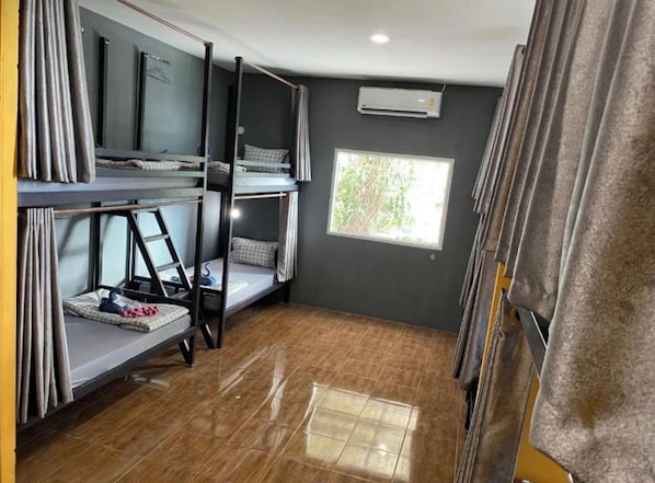 A dormitory room with bunk beds, a window with a view of trees, and an air conditioning unit on the wall. - The View Hostel (Ko Phi Phi)