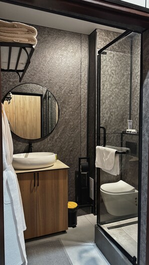 A modern bathroom with a wooden vanity, a round mirror, a glass-enclosed shower, and a toilet. - AIRIS RESIDENCE hotel (Almaty)