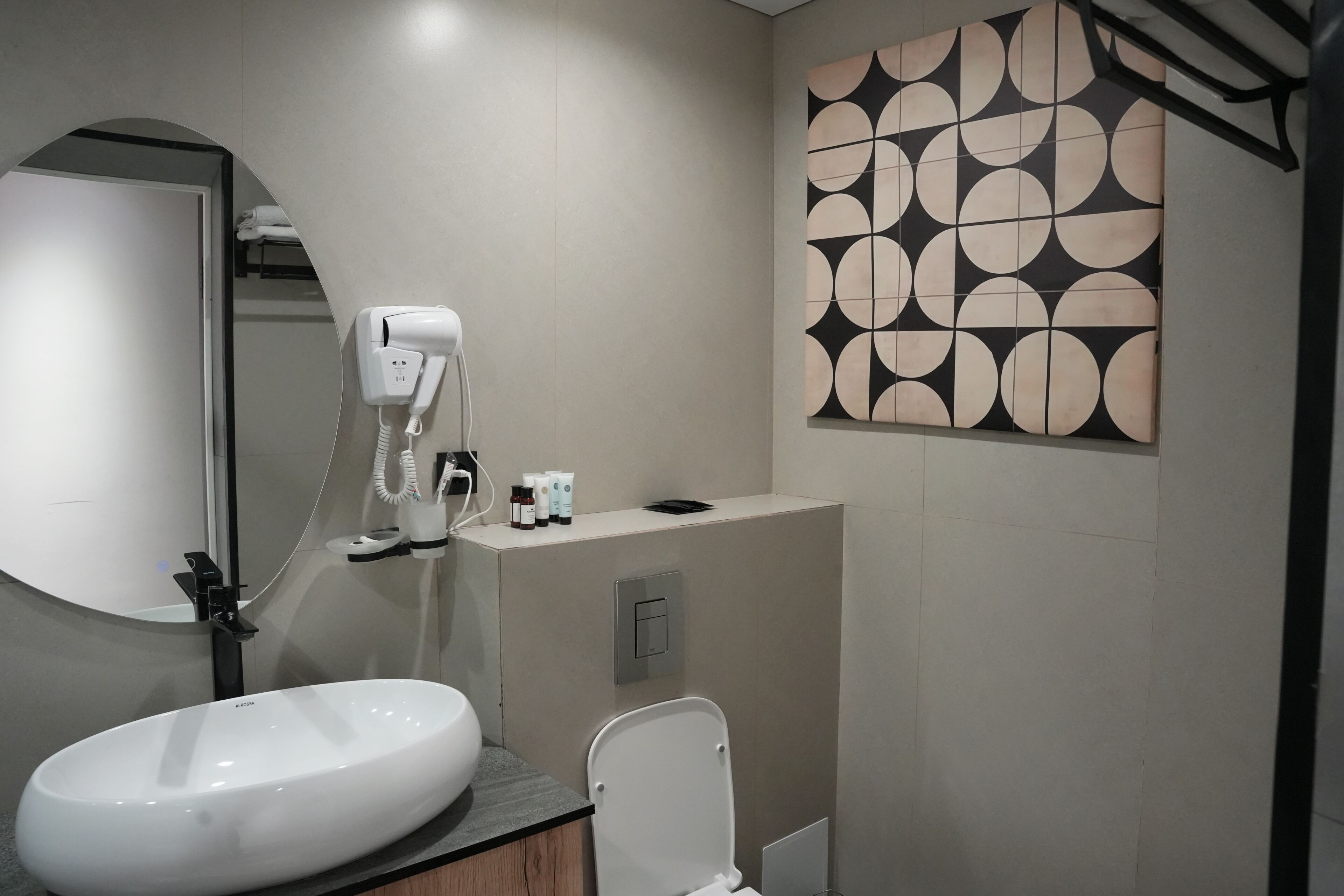 Un baño moderno con un lavamanos ovalado grande, un secador de pelo de mano, un inodoro y un toallero de pared.