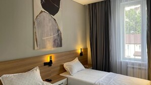 A hotel room with two single beds, a wooden headboard, a wall-mounted artwork, and a window with curtains. - AIRIS RESIDENCE hotel (Almaty)