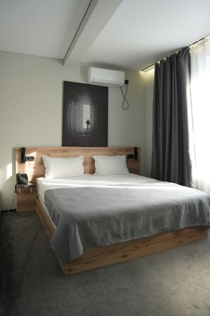 Camera d'albergo moderna con testiera in legno, un letto singolo, un telefono sul comodino e un condizionatore d'aria a parete.