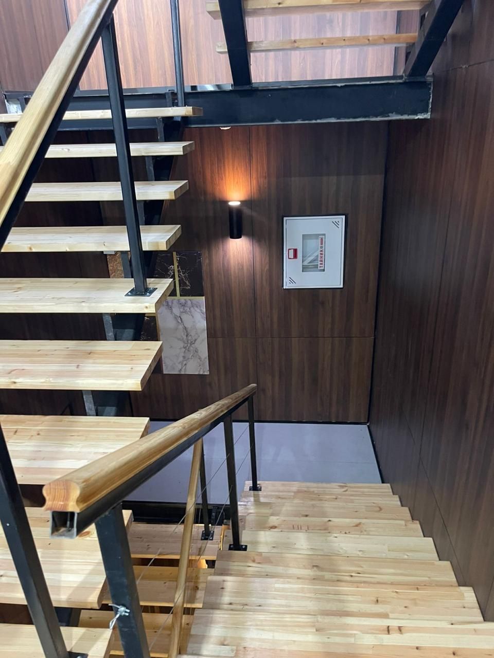 Una escalera de madera con barandillas de metal, una luz fijada a la pared y un cuadro enmarcado.