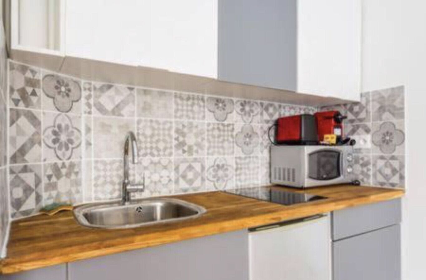 A kitchen with a wooden countertop, a stainless steel sink, and a microwave on the counter.