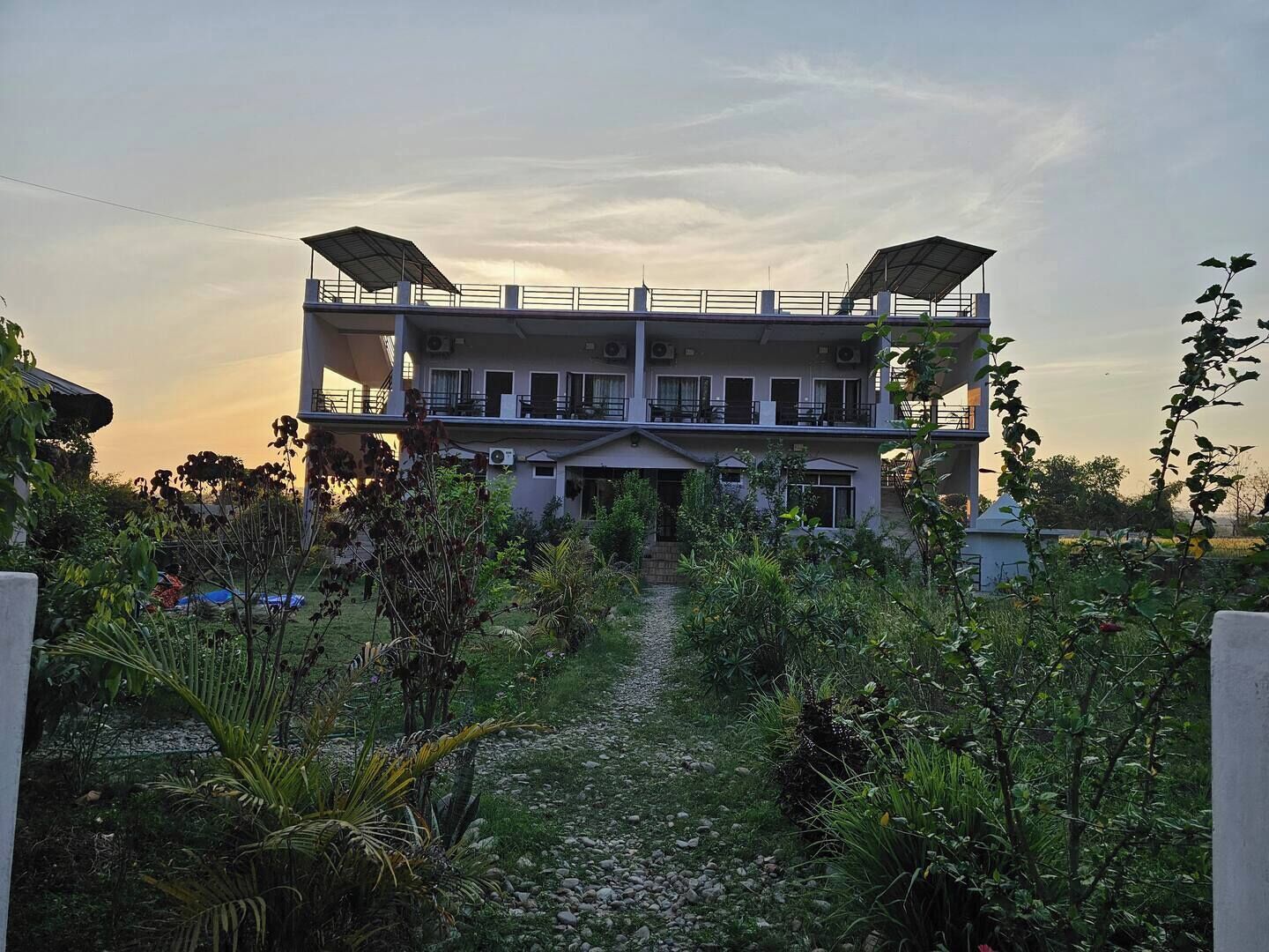 A two-story building with a central courtyard, surrounded by greenery and a gravel path.