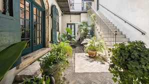 A narrow courtyard with a staircase leading to an upper level, surrounded by potted plants and a rustic stone floor. - The Master Suite - A spacious suite inspired by Charleston’s grace and charm (Charleston)